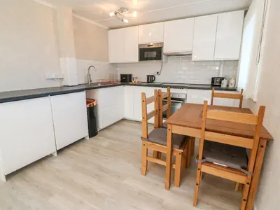 a kitchen with white cabinets and a wooden table and chairs at Valhalla in St Ives