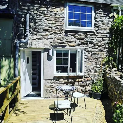 a table and chairs on a wooden deck in front of a stone house at 1 Bed Cottage-Sleeps 3-Pool-Pets-near St Ives in Camborne