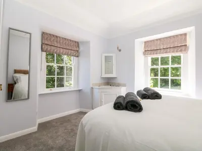 a white bedroom with a bed and two windows at Culdrose Manor in Helston