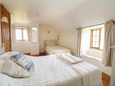 a bedroom with two beds and a window at Higher Roskorwell Cottage in Helston