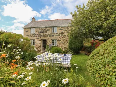 a stone house with a table and chairs in the garden at Higher Roskorwell Cottage in Helston
