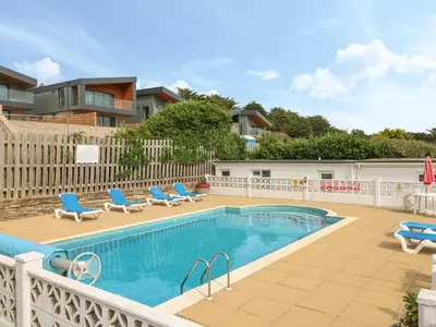 a swimming pool with blue lounge chairs and a house at 2 Europa Court in Newquay
