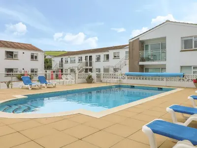 a swimming pool with blue chairs next to a building at 2 Europa Court in Newquay