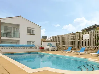 a swimming pool with two blue chairs and a house at 2 Europa Court in Newquay