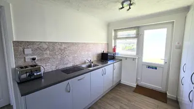 a kitchen with white cabinets and a sink and a window at 10 Wheal Ramoth in Perranporth