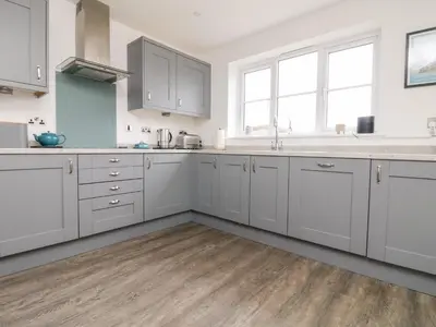 a kitchen with white cabinets and a wooden floor at Beacon House in St. Agnes