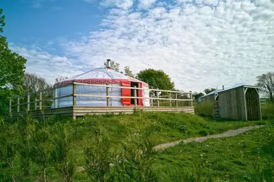 a red building in a field with a house at Glamping Yurts near Newquay in Newquay