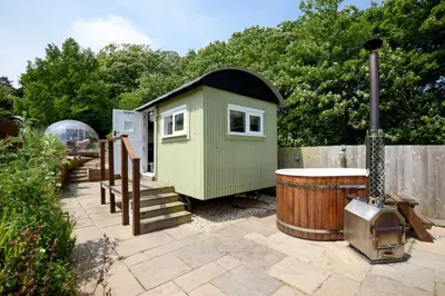a small green house and a barrel in a yard at Luxury Coastal Shepherds Hut with hot tub, dining dome & a 5 Minute Walk to Pubs and Village in Polperro