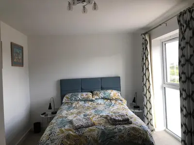 a bedroom with a bed with a blue headboard and a window at 2 Lapwing Drive in Hayle