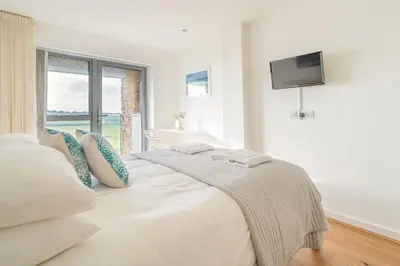 a white bedroom with a bed with a tv on the wall at Newquay Fistral Beach View in Newquay