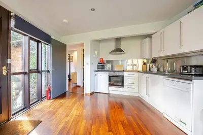 a kitchen with white cabinets and a wooden floor at Charming Summerhouse Annexe in lush gardens in Fowey in Fowey