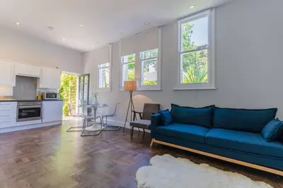 a living room with a blue couch and a kitchen at Classroom Flat Suite in a converted school in Fowey town centre in Fowey