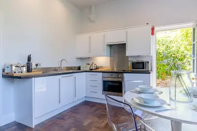 a kitchen with white cabinets and a table with chairs at Classroom Flat Suite in a converted school in Fowey town centre in Fowey