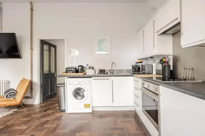 a kitchen with white cabinets and a washer and dryer at Classroom Flat Suite in a converted school in Fowey town centre in Fowey