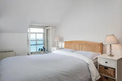 a white bedroom with a bed and a window at Trevarrow Cottage in Coverack