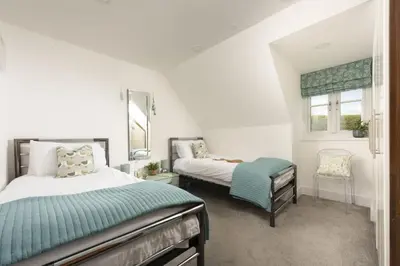a bedroom with two beds and a chair at 10 The Whitehouse, Watergate Bay in Mawgan Porth