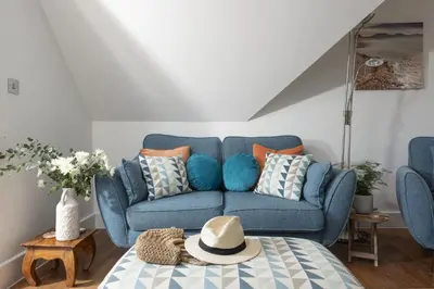 a blue couch in a living room with a hat on a table at 10 The Whitehouse, Watergate Bay in Mawgan Porth