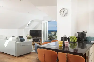 a kitchen and living room with a clock on the wall at 10 The Whitehouse, Watergate Bay in Mawgan Porth