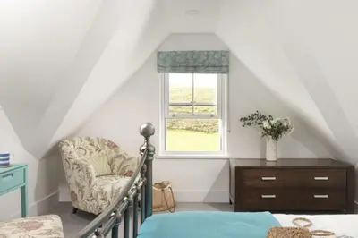a bedroom with a bed and a chair and a window at 10 The Whitehouse, Watergate Bay in Mawgan Porth