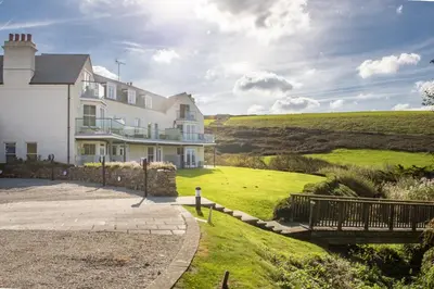 a large white house with a green field behind it at 10 The Whitehouse, Watergate Bay in Mawgan Porth