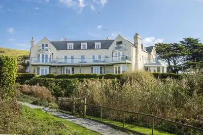 a large white house on a hill with a fence at 10 The Whitehouse, Watergate Bay in Mawgan Porth