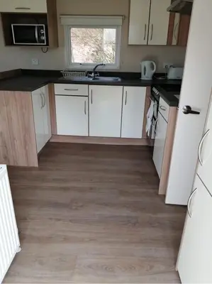 a kitchen with white cabinets and a wooden floor at 67 Newquay Getaway in Porth
