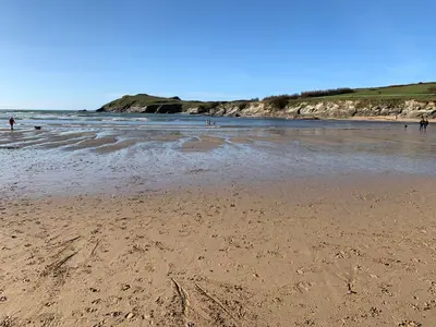 a sandy beach with people walking in the water at Newquay Bay in Newquay