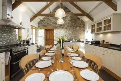 a large kitchen with a long wooden table and chairs at Mowhay Barn - Woodburner & Hot tub in Padstow