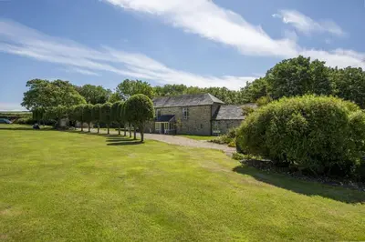 an old stone house with a row of trees at Mowhay Barn - Woodburner & Hot tub in Padstow