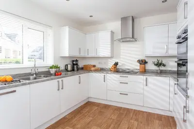 a white kitchen with white cabinets and wood floors at Endymion in Porthtowan