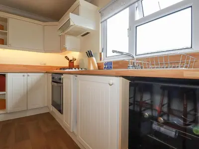 a kitchen with white cabinets and a sink and a window at Summer Breeze in Padstow