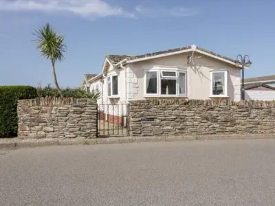 a white house with a stone wall and a palm tree at Summer Breeze in Padstow