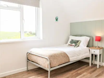 a white bedroom with a bed and a window at Pepperpots in Newquay