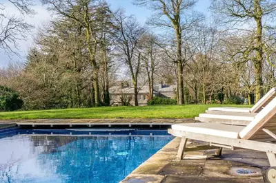 a swimming pool with a bench next to a house at The Manor House at Boconnion in Bodmin