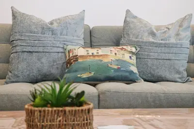 a couch with pillows with a painting of a harbor at NEAR BEACHES, contemporary home in village centre in St Merryn