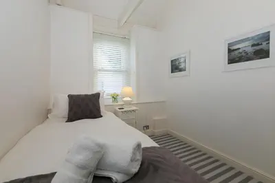 a white bedroom with a bed and a window at Breaking Waves in St Ives