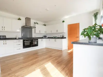 a kitchen with white cabinets and a wooden floor at Penn-An-Vownder in Newquay