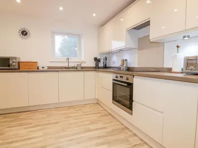 a kitchen with white cabinets and a wooden floor at Lily Cottage in Camelford