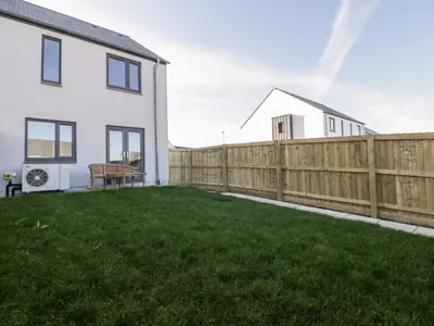 a backyard with a wooden fence and green grass at The Sand Dunes in Crantock