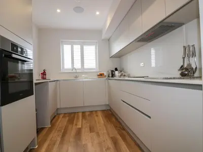 a kitchen with white cabinets and a wooden floor at The Sand Dunes in Crantock