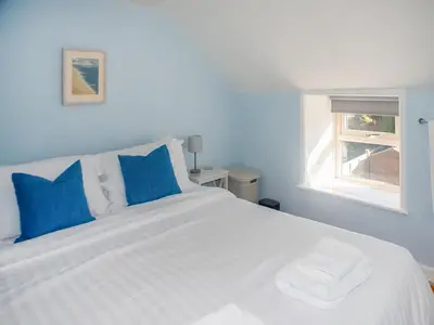 a white bed with blue pillows and a window at Little Trevarrack in Carbis Bay