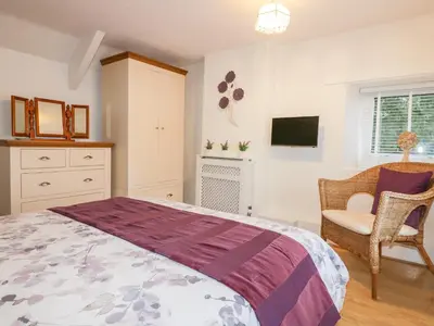 a bedroom with a bed and a chair and a tv at Hawthorn Cottage in Bodmin