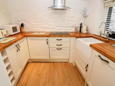 a kitchen with white cabinets and a wooden floor at Bay Tree Cottage in Looe
