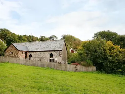 an old stone barn in a field with a fence at Frogwell Chapel in Callington