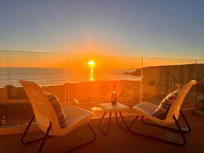 two chairs and a table on a balcony with a sunset at Sea Sands in Penzance