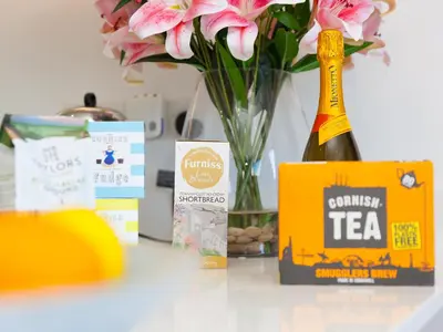 a table with a vase of flowers and a bottle of tea at Sea Sands in Penzance