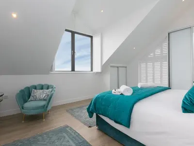 a white bedroom with a bed and a chair at Sea Sands in Penzance