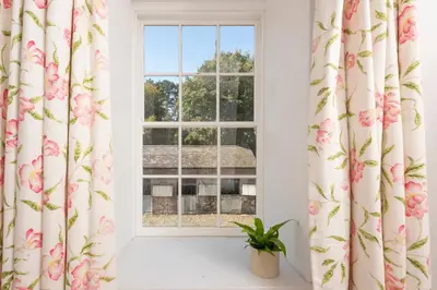 a window with pink flower curtains and a potted plant at Stable House in Redruth