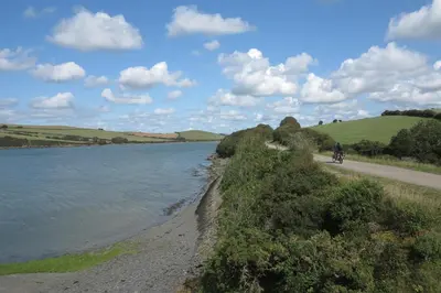 a person riding a bike on a path next to a body of water at Edge of Padstow, 2 bedroom luxury lodge in Padstow