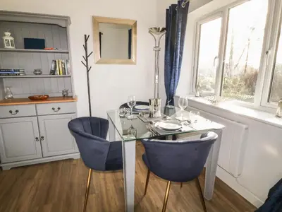 a dining room with a glass table and blue chairs at Primrose End in Bude